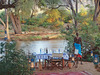 Elephant Watch Camp, a local tribesman stands near the dinner table set up along the banks of a secluded river for a private experience, Kenya