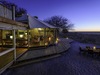 Khalahari Plains Camp, indoor/outdoor lounge area, dining table on sandy area, extensive surrounding wood deck for great views, dusk in Africa